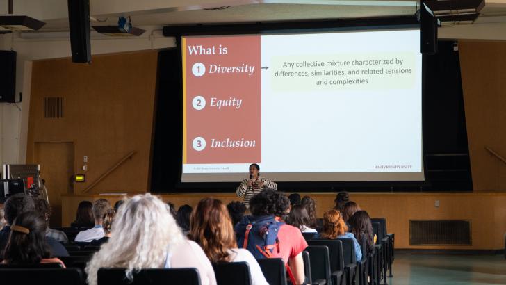 presenter speaking to group in auditorium with Diversity, Equity, and Inclusion on projector screen