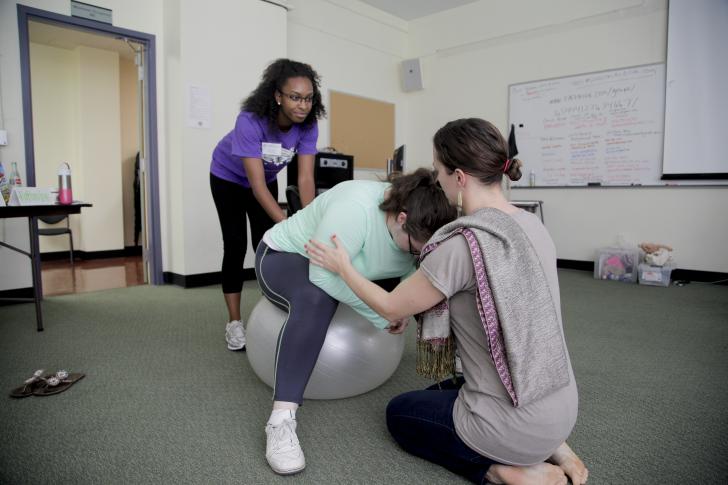 two students helping pregnant person in birth class